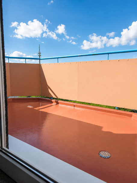 Blick auf einen leeren Balkon mit orangefarbenem Boden und blauen Himmel.
