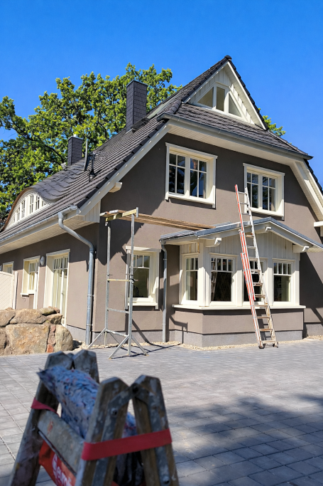 Renoviertes Haus mit Gerüst und Leiter vor blauem Himmel.