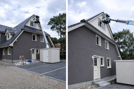 Ein graues Haus mit einem geräumigen Dach, auf dem eine Arbeitsmaschine eingesetzt wird.