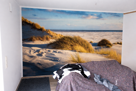 Schlafzimmermit Sanddünen und Graslandschaft auf der Wand, Couch im Vordergrund.